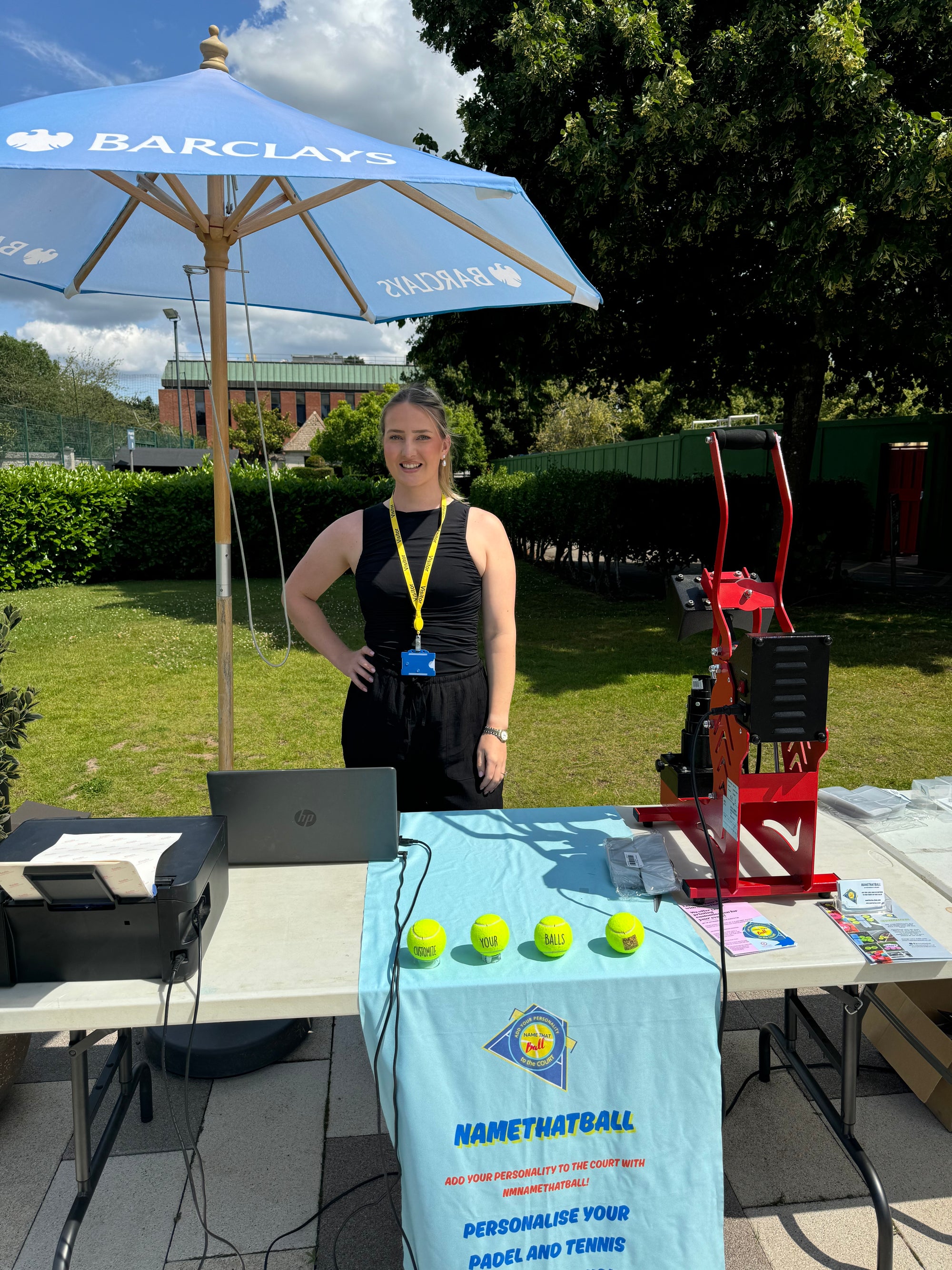 standing outdoors with a Barclays umbrella and sports equipment on a table.